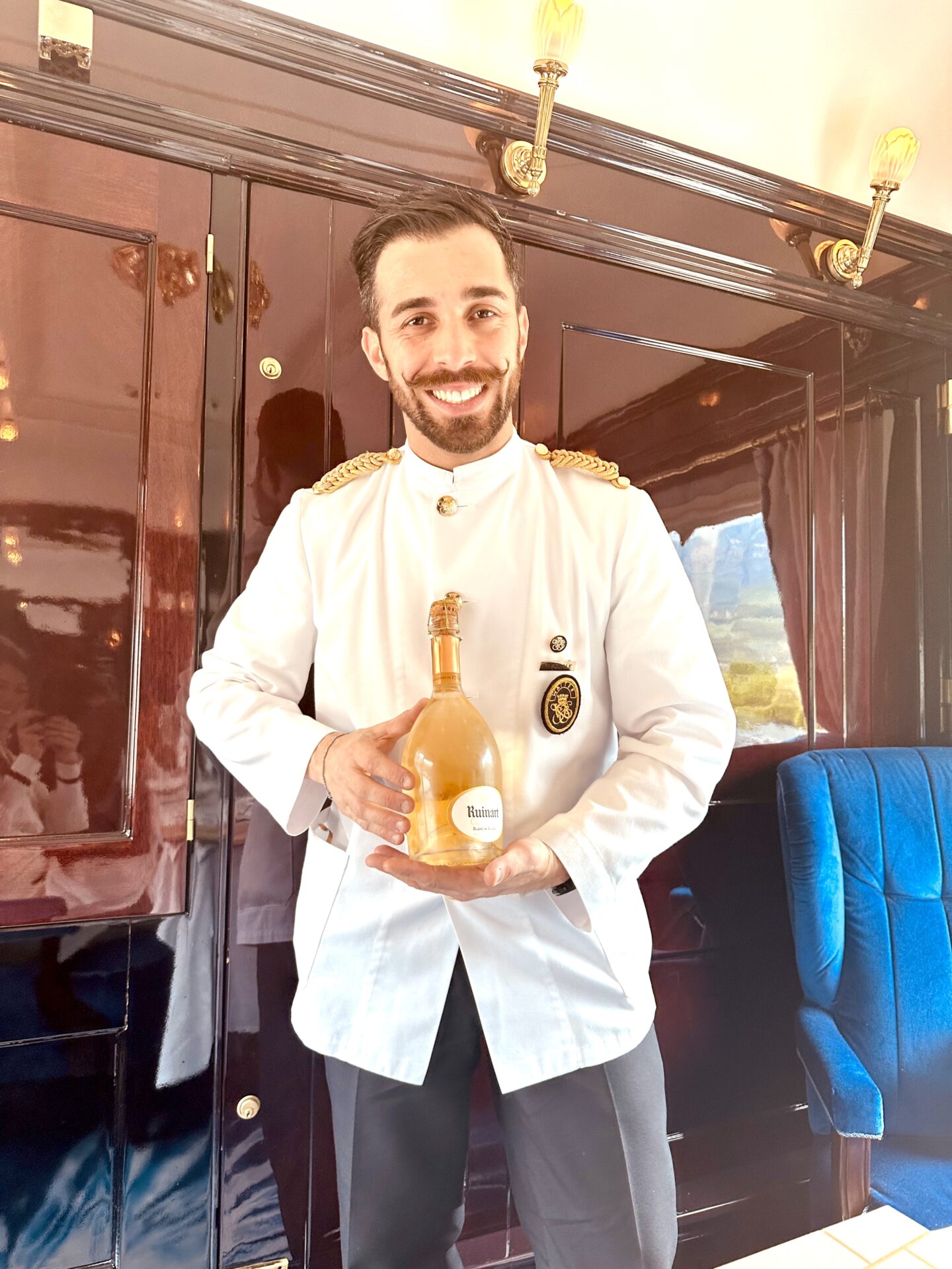orient express first class - butler in white uniform holding Ruinart champagne aboard the Venice Simplon-Orient-Express.